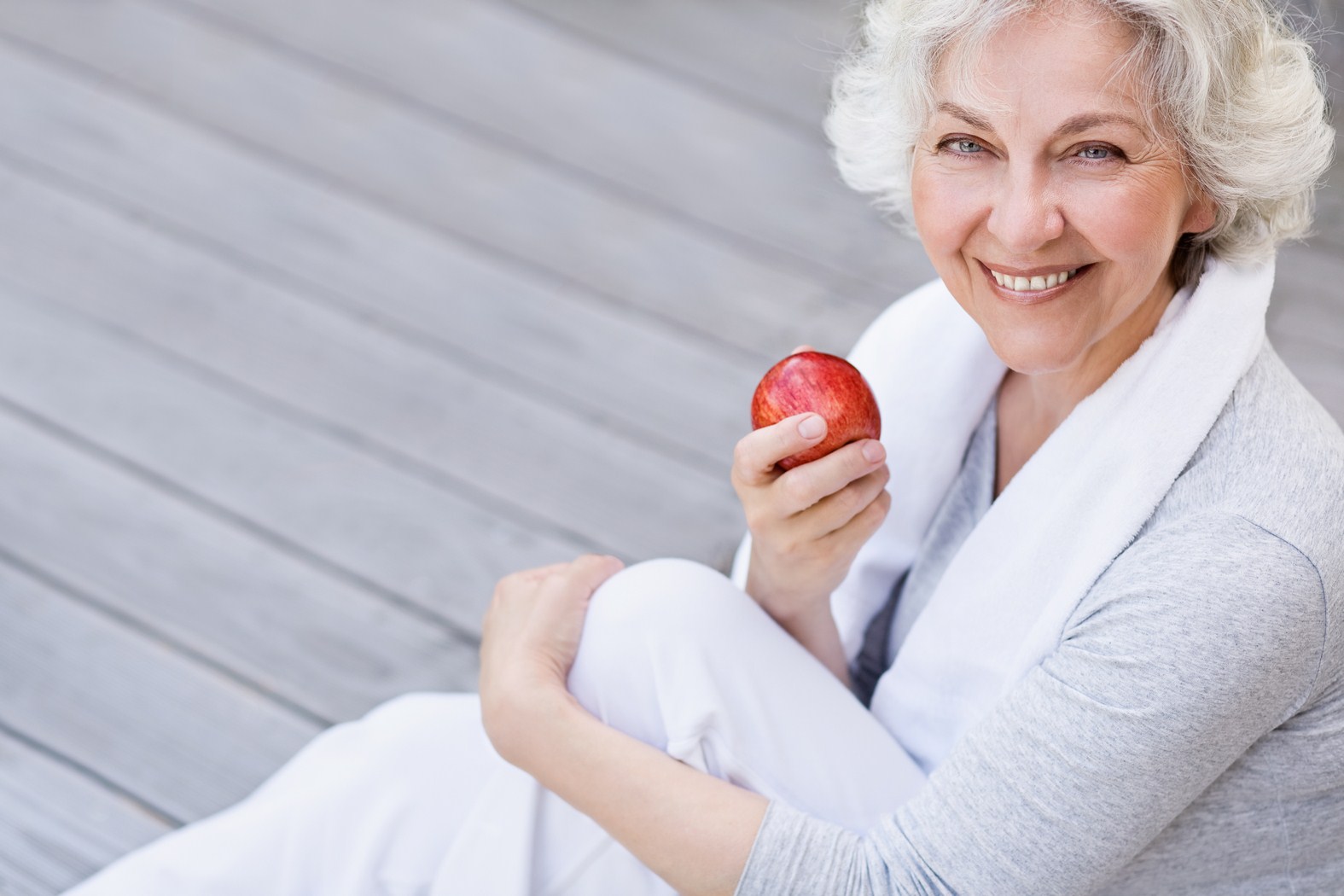 Grauhaarige Frau mit rotem Apfel guckt glücklich